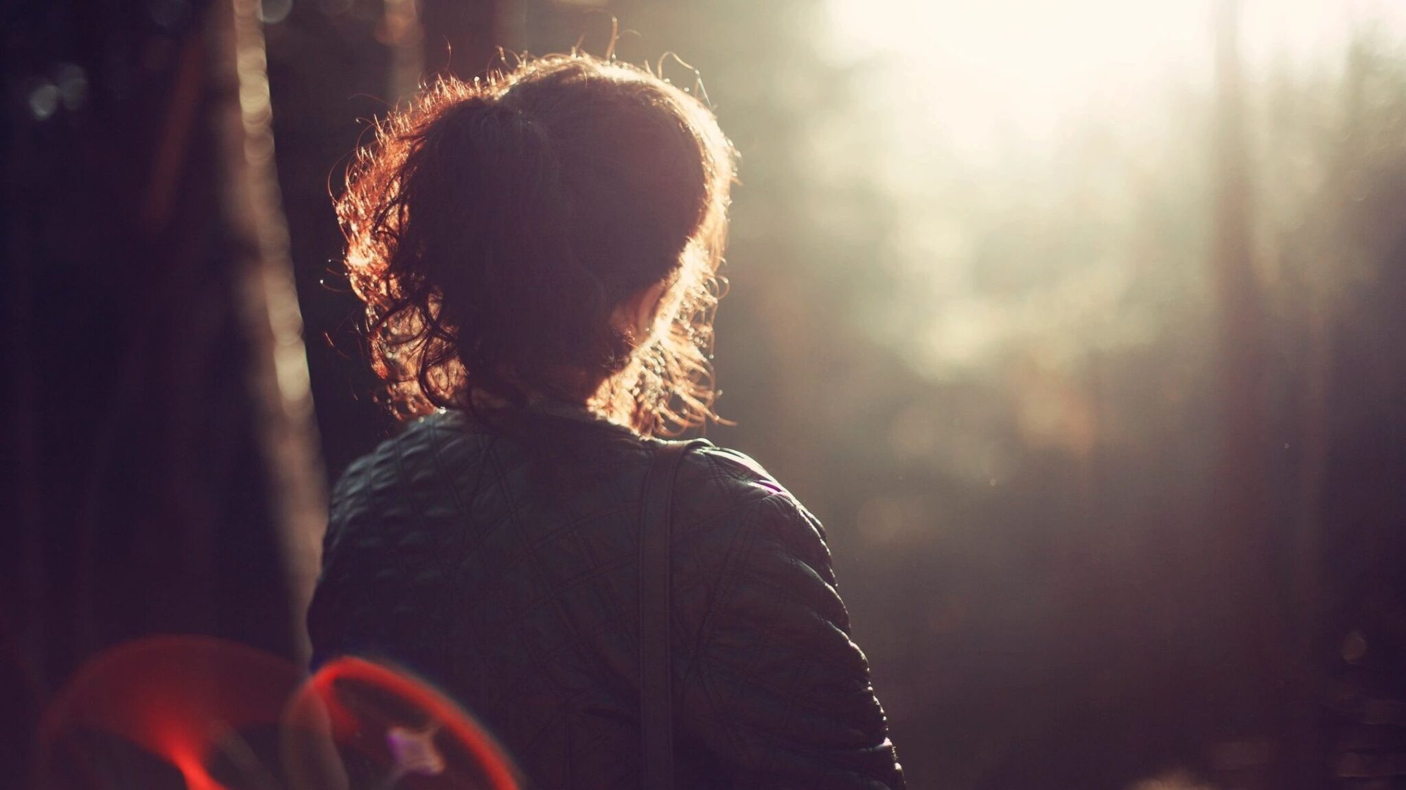 A lady watches the sunset in a wooded area.