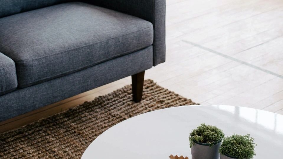 The corner of a grey couch  with a white coffee table in front of it with two plants on top of the table.